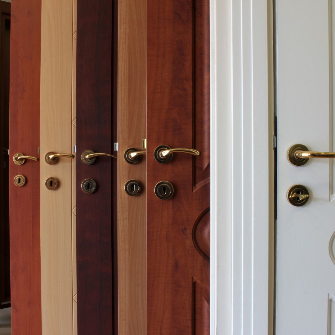 A collection of different door types stacked together in an organized manner, showcasing a variety of designs including modern, classic, and minimalist styles, made from materials like wood, glass, and metal, set against the backdrop of a workshop.
